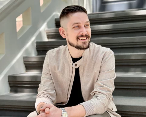 Ben Carr sitting on a set of gray steps under dappled light, looking slightly off camera